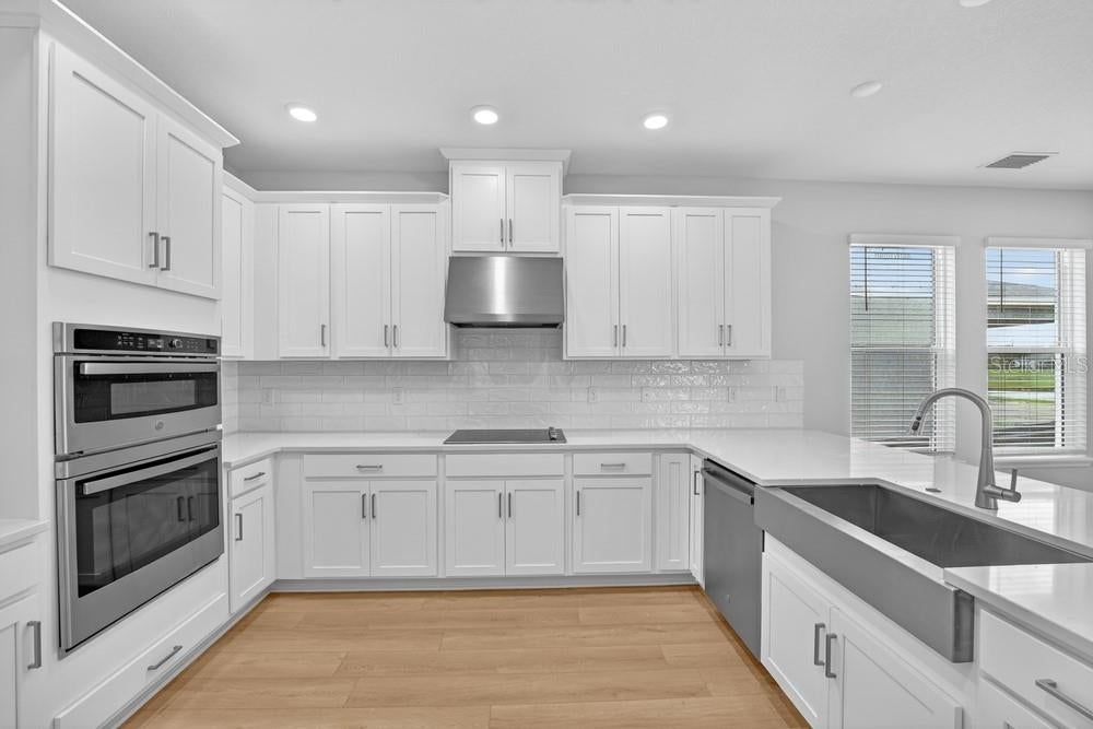 Anastasia kitchen detail showing farmhouse sink, double ovens, and subway tile backsplash